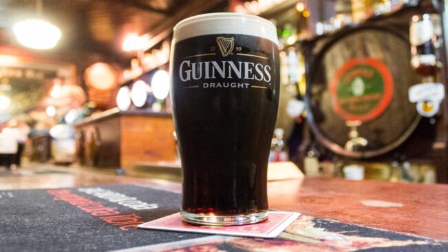 Kufel ciemnego piwa Guinness na barze z beczką w tle